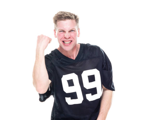 One man only / waist up of 20-29 years old adult handsome people caucasian male / young men fan - enthusiast / american football player in front of white background wearing jeans / sports uniform / sports clothing who is excited / happy / cheerful / success / smiling and cheering who is and doing fist pump and holding ball / support / american football - sport / sport / american football - ball un hombre sólo / cintura para arriba de 20-29 años de edad adulto guapo personas caucásicas hombres / jóvenes fan - entusiasta / jugador de fútbol americano frente a fondo blanco usando jeans / uniforme deportivo / ropa deportiva y animando y sostenie