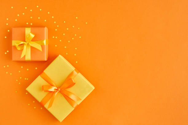 две подарочные коробки с лентой и луком на оранжевом фоне с золотыми звездами. вид сверху и пространство для текста. - yellow box стоковые фото и изображения