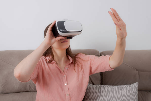 istock Woman using VR sitting on couch holding handset with one hand having the sensation of touching some virtual object. 1172806722