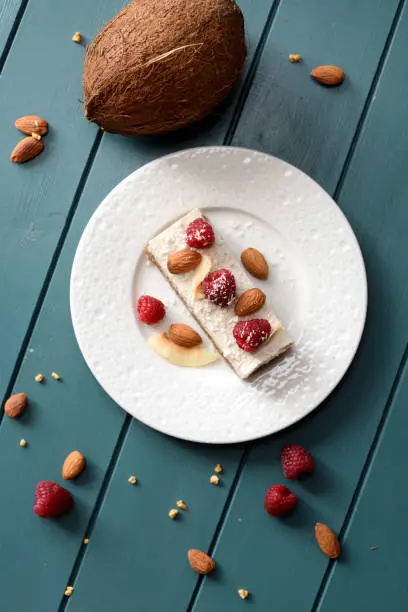 Healthy sugar free vegan dessert. Coconut milk cheesecake with raspberries and almonds and whole coconut on dark background top view copy space