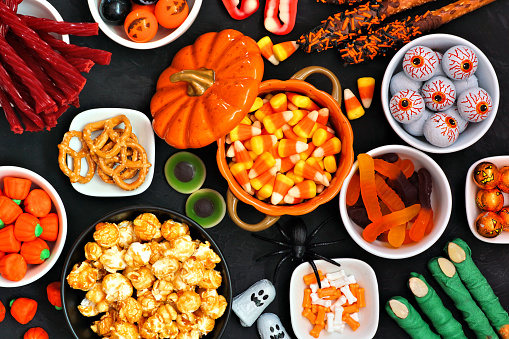 Halloween candy buffet table scene over a black stone background. Assortment of sweet, spooky treats. Above view.