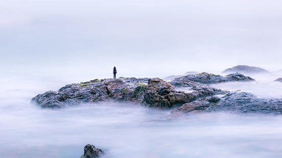 Magic landscape with lone person and surreal rocks in sea. Long exposure of mystery ocean and stones. Fantastic view of water like fog, mist or clouds. Beautiful mystic panorama of marine nature.