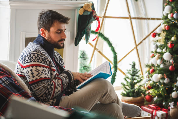 istock Man reading a book at home by the Christmas tree 1172836738