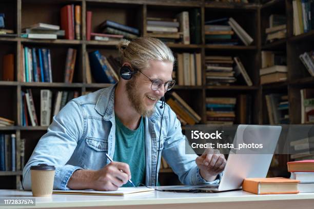 Sonriente Feliz Joven Usando Auriculares Inalámbricos Mirar La Pantalla Del Ordenador Portátil Hacer Que Las Notas Estudian E Aprendizaje En La Biblioteca Ver Webinar Curso De Vídeo De Vídeo Educación A Distancia Concepto De Enseñanza Skype Foto de stock y más banco de imágenes de Cámara de vídeo