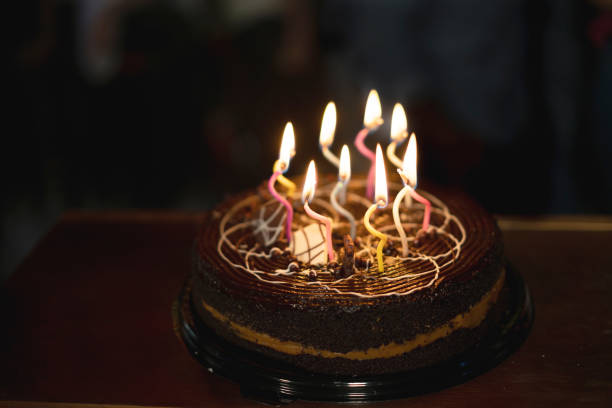 Birthday cake with white whipped cream, meringues and cranberries, decorated with multicolored lit candles. Happy Birthday concept. Tradition of making a wish blowing out candles. Selective focus.