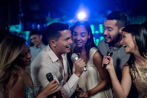 Happy group of Latin American friends having fun singing at a karaoke bar - lifestyle concepts