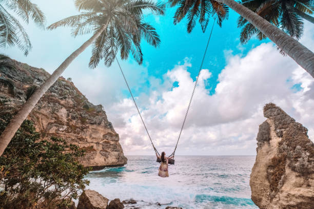 belle fille sur les paumes de noix de coco de balancement sur la plage à la plage de daimond, île de nusa penida bali, indonésie - bali photos et images de collection