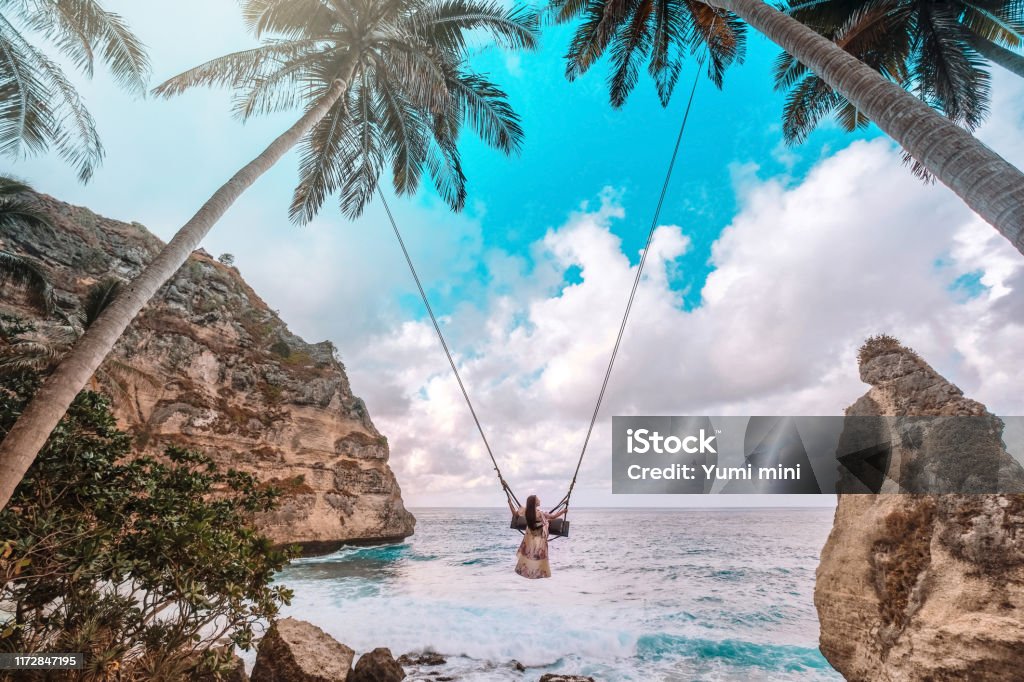 Beautiful girl on swing coconut palms on beach at Daimond  beach, Nusa Penida island Bali ,Indonesia Bali Stock Photo