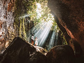 Traveling young couple with tropical rainforest rock in Bali enjoying life at beautiful Lighting hidden waterfall.