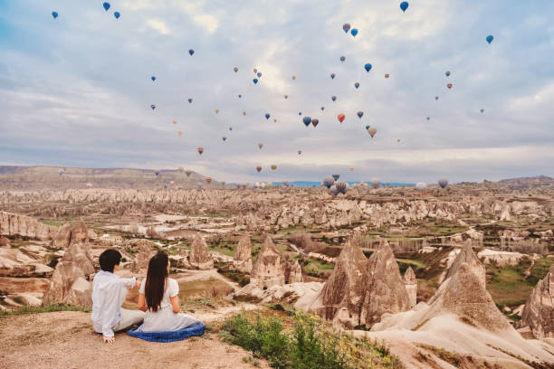 asian couple watching colorful hot air balloons flying over the valley at cappadocia, turkey this romantic time of love - cappadocia hot air balloon turkey basket imagens e fotografias de stock