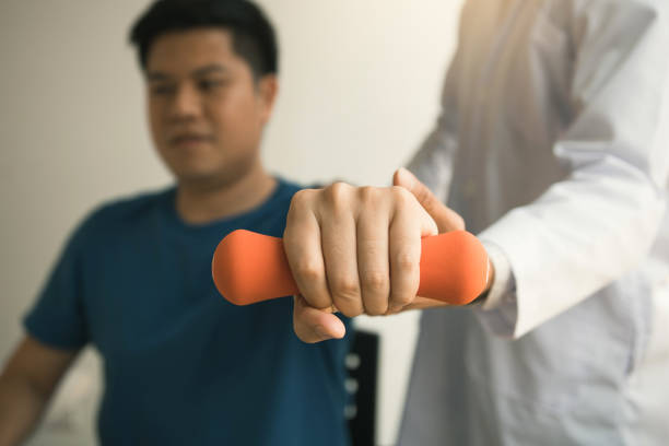 istock Asian physiotherapist helping a patient lifting dumbbells work through his recovery with weights in clinic room. 1172847407