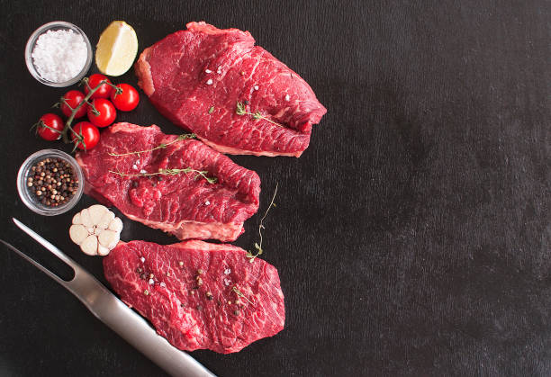 Fresh raw beef steak Mignon, with salt, pepper, thyme, tomatoes on a black wooden table. The view from the top. Copy space