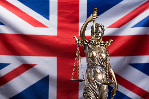 The statue of justice Themis or Justitia, the blindfolded goddess of justice against a flag of the United Kingdom