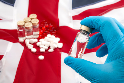 Medicine shortages, stockpile drugs and medical crisis as result of no deal brexit concept theme with doctor wearing latex gloves holding a vaccine with the UK flag in background and other medicines