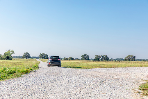 Small vehicle driving down gravel road in pasture on Texas farm