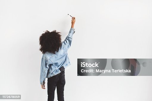 istock A dark-skinned girl stands near the wall and writes something. 1172878059