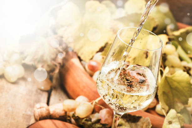 White wine being poured into a glass, vintage wood background, selective focus stock photo