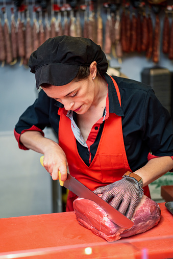 Female butcher cutting fresh meat in a butcher shop with metal safety mesh glove