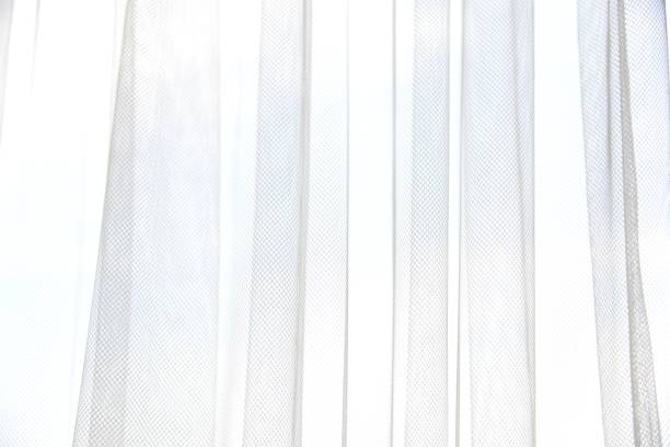 istock White tulle curtain with vertical folds. Window with light curtains. Soft textile texture. Light and shadow abstract background. 1172882729