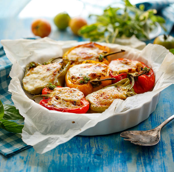 Baked multi-colored bell peppers stuffed with bulgur with dried tomatoes, herbs and cheese in a baking dish on a blue table.Vegetarian dish, stuffed vegetables