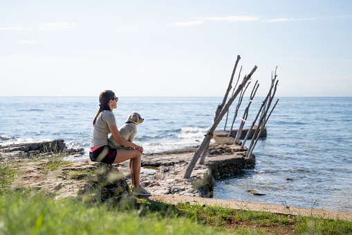 Adult Woman Relaxing on Coastline With Her Dog and Looking at View.