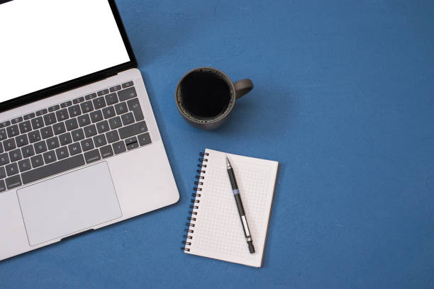 istock Top view workspace mockup, blank screen laptop, coffee mug, notepad and pencil on blue texture desk 1172899878