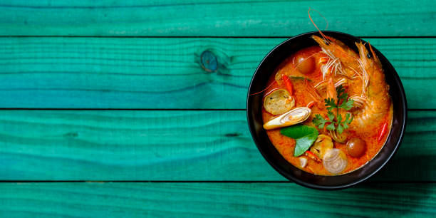 tajlandia słynnego bogatego, czerwonego, na bazie mleka kokosowego, pysznej zupy tom yam kung w misce na abstrakcyjnym turkusowym kolorze zwiewnym drewnianym tle stołu. - thailand thai cuisine prawn tom yum soup zdjęcia i obrazy z banku zdjęć