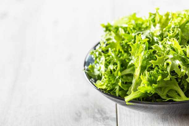 Fresh salad endivia in black bowl on wooden table.
