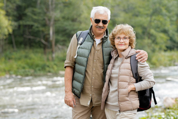 istock Happy mature active couple with backpacks looking at you by forest river 1172918104