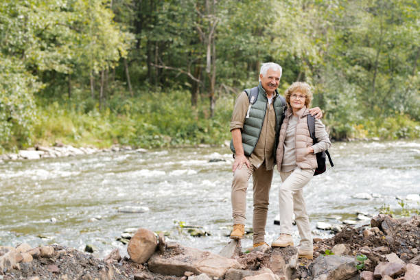 istock Affectionate mature spouses with backpacks standing on stones on river bank 1172918120