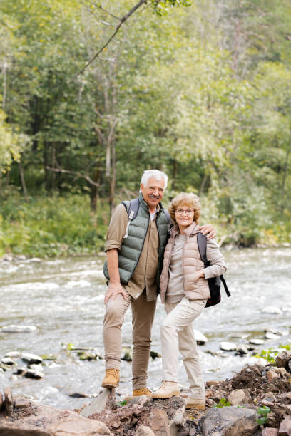 istock Happy aged active hikers with backpacks looking at you while standing by river 1172918121