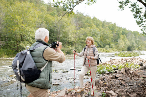 istock Active female hiker with trekking sticks looking at husband with camera on trip 1172918155
