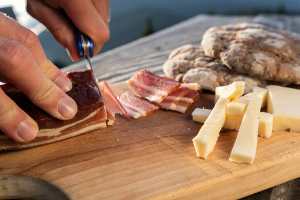 istock Man slice up delicious South Tyrolean smoked bacon and cheese with flat bread lying on a rustic table 1172923092