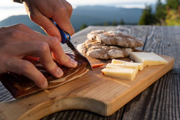 istock Man slice up delicious South Tyrolean smoked bacon and cheese with flat bread lying on a rustic table 1172923393
