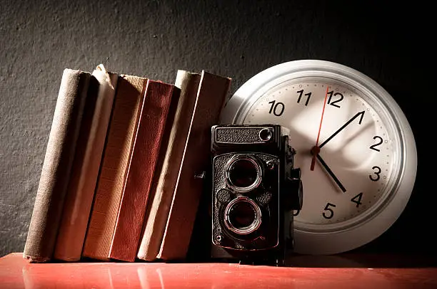 Old camera, old books and a clock on bookshelf.