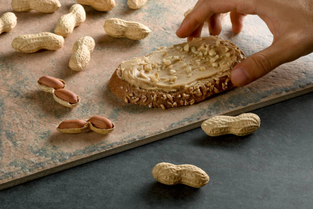 A male hand holding peanut butter bread with shelled peanuts