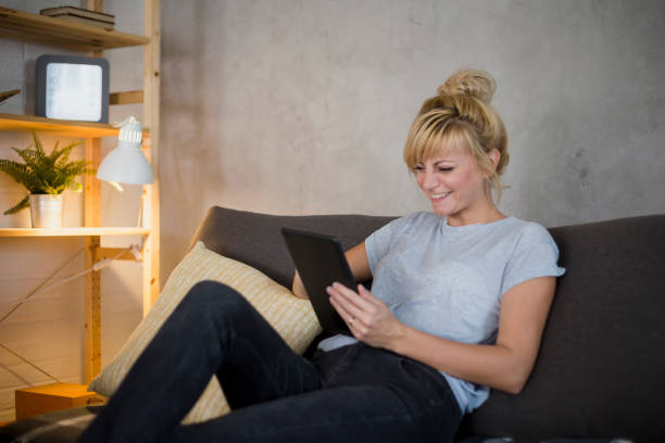 istock Young woman browsing on tablet. She is sitting on sofa in modern living room. 1172957723