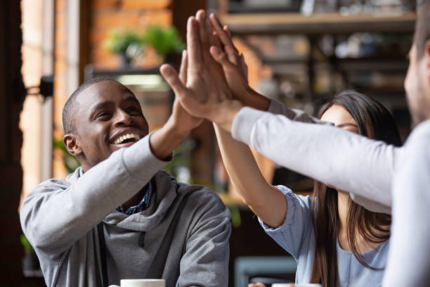 istock Cheerful different ethnicity friends sitting in cafe giving high five 1172964135