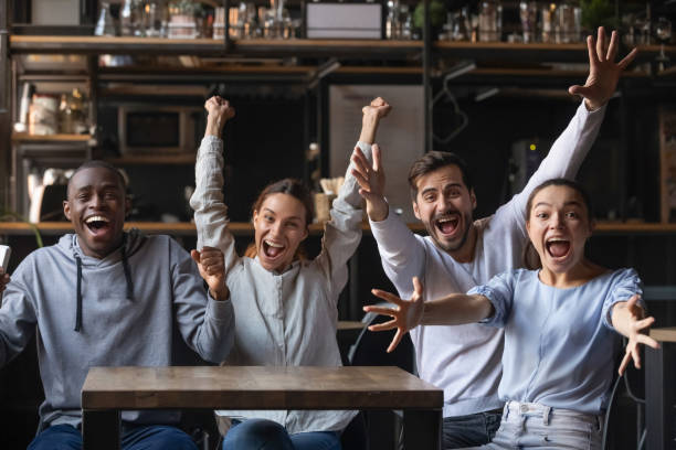 Diverse overjoyed football fans looking at camera screaming feels happy Multi-ethnic people looking at camera sitting at cafe public place screaming shouting feels overjoyed happy by favourite football club team winning get victory, sports betting, lottery winners concept cheering group of people success looking at camera stock pictures, royalty-free photos & images