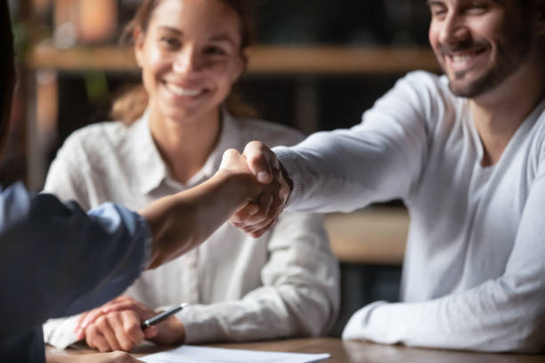 millennial fröhliche geschäftsleute schütteln hände sitzend drinnen - adult businesswoman greeting human hand stock-fotos und bilder