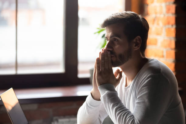 Concerned serious doubtful man sitting near laptop and thinking