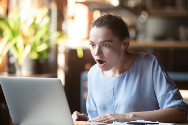istock Female reading message on computer open mouth feels surprised amazed 1172964271