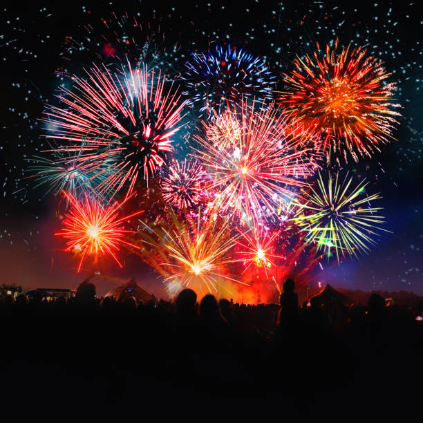 crowd cheering in front of vibrant firework silhouettes of human crowd cheering in front of vibrant firework under night sky firework colors stock pictures, royalty-free photos & images