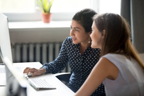 Smiling female colleagues work together at computer Smiling multiracial millennial girls look at screen work at computer in office together, young diverse female colleagues cooperate using pc, browsing internet or reading news. Collaboration concept indian girl from the office stock pictures, royalty-free photos & images