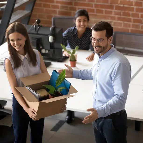 Smiling male CEO or boss introduce excited millennial woman employee to office colleagues, happy newcomer hold belongings box get acquainted with coworkers on first work day, welcome in team