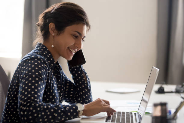 smiling employee working on laptop talking over phone - retail occupation customer advice imagens e fotografias de stock