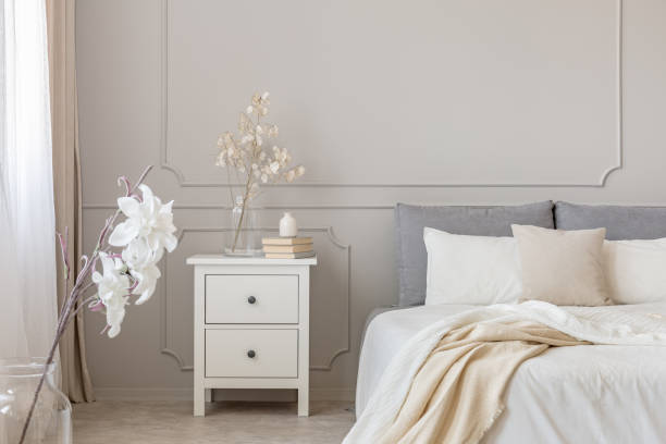 Flowers on nightstand table in delightful bedroom interior with grey and white design