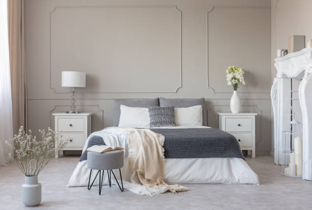 istock Flowers on nightstand table in delightful bedroom interior with grey and white design 1172970024