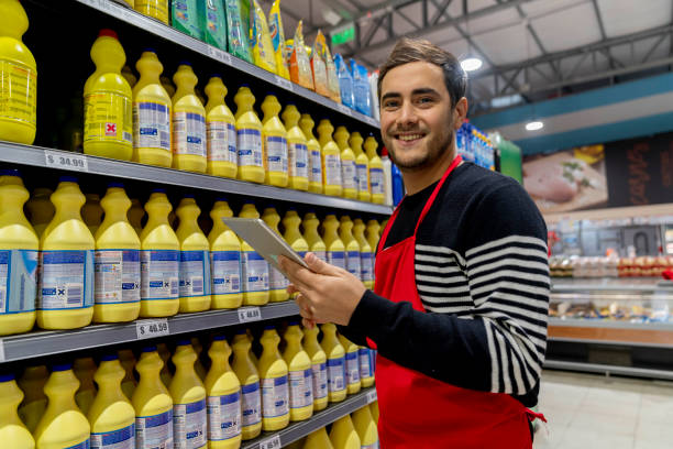 hombre latinoamericano trabajando en el supermercado sosteniendo un portapapeles haciendo inventario de los productos de limpieza en estante sonriendo a la cámara - men latin american and hispanic ethnicity young men smiling fotografías e imágenes de stock