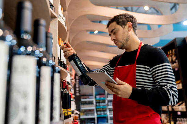 ラテンアメリカ人の男性は、タブレットを保持し、ワインブランドを見て、オンライン注文を準備します - liquor store ストックフォトと画像